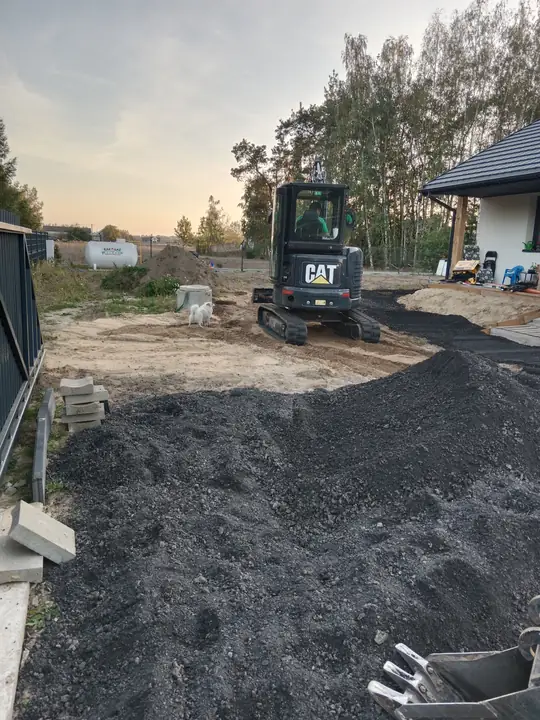 Podjazd z kruszywa widziany od bramy, koparka w głębi