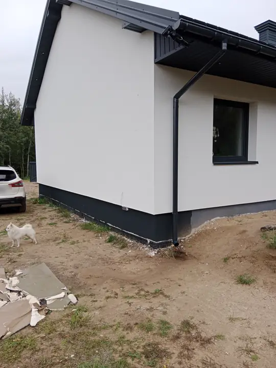 Narożnik domu z rynną kończącą się nad piaskiem